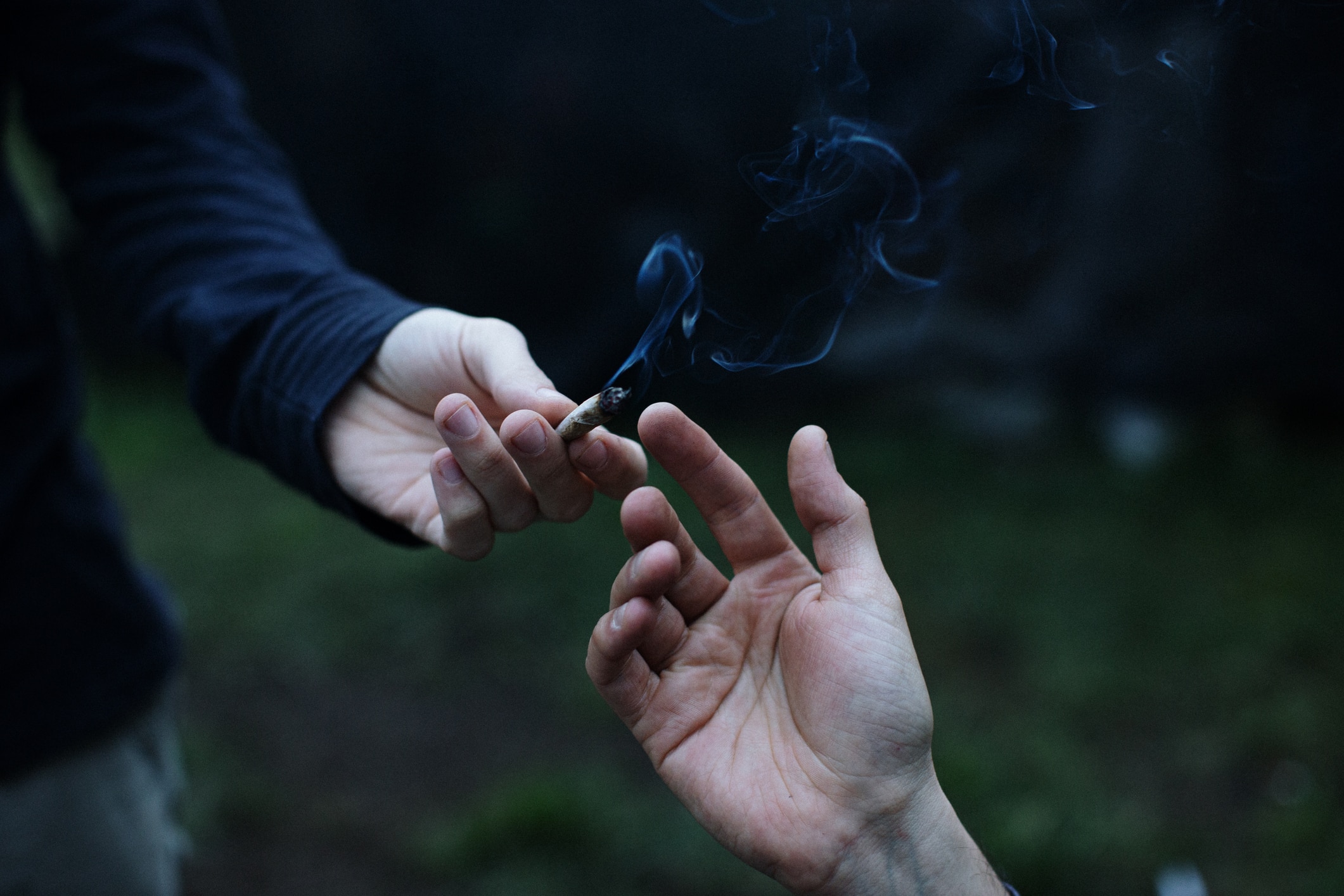 two hands passing a cannabis joint